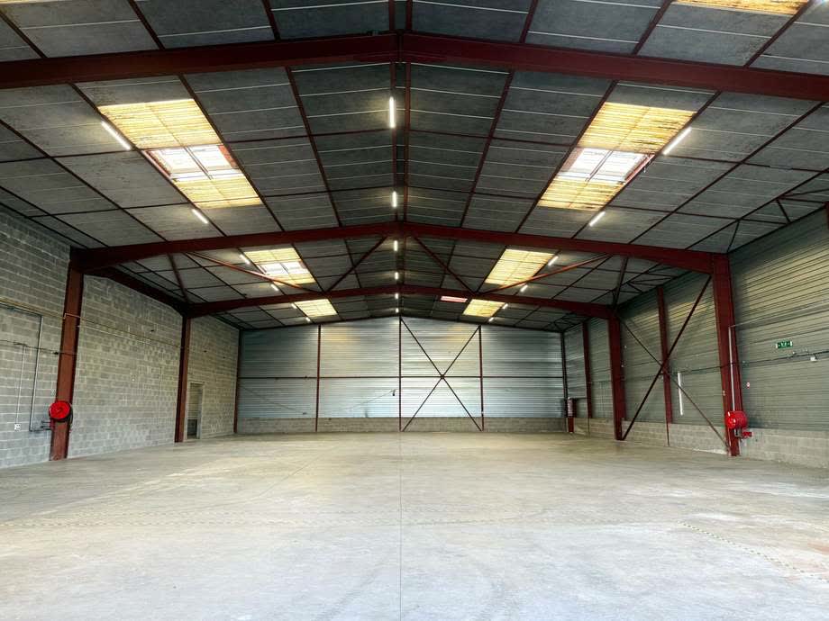 Intérieur vacant du bâtiment de l’avenue de Lattre de Tassigny : charpente métallique rouge, portes sectionnelles et éclairage zénithal.